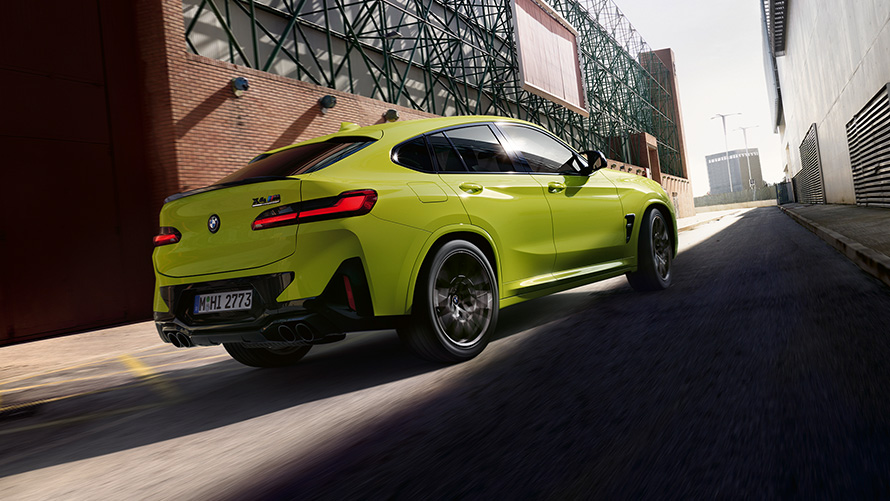 BMW X4 M Competition F98 LCI Facelift 2021 Sao Paulo Gelb vue de trois quarts arrière roulant entre des bâtiments d’usine